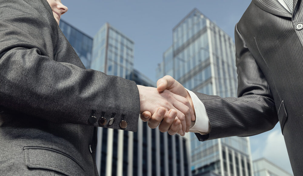 Businessmen shake hands with each other. Zodia Markets Standard Chartered plans to acquire Elwood's OTC crypto unit.