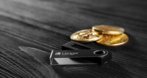 Ledger hardware wallet on wood background next to a stack of golden Bitcoin coins.