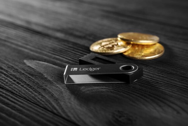 Ledger IPO Ledger hardware wallet on wood background next to a stack of golden Bitcoin coins.